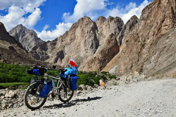 Rower z sakwami i polską flagą na tle gór Pamiru. To inspiracja, jak zaplanować logistykę wyprawy rowerowej przez Pamir Highway.